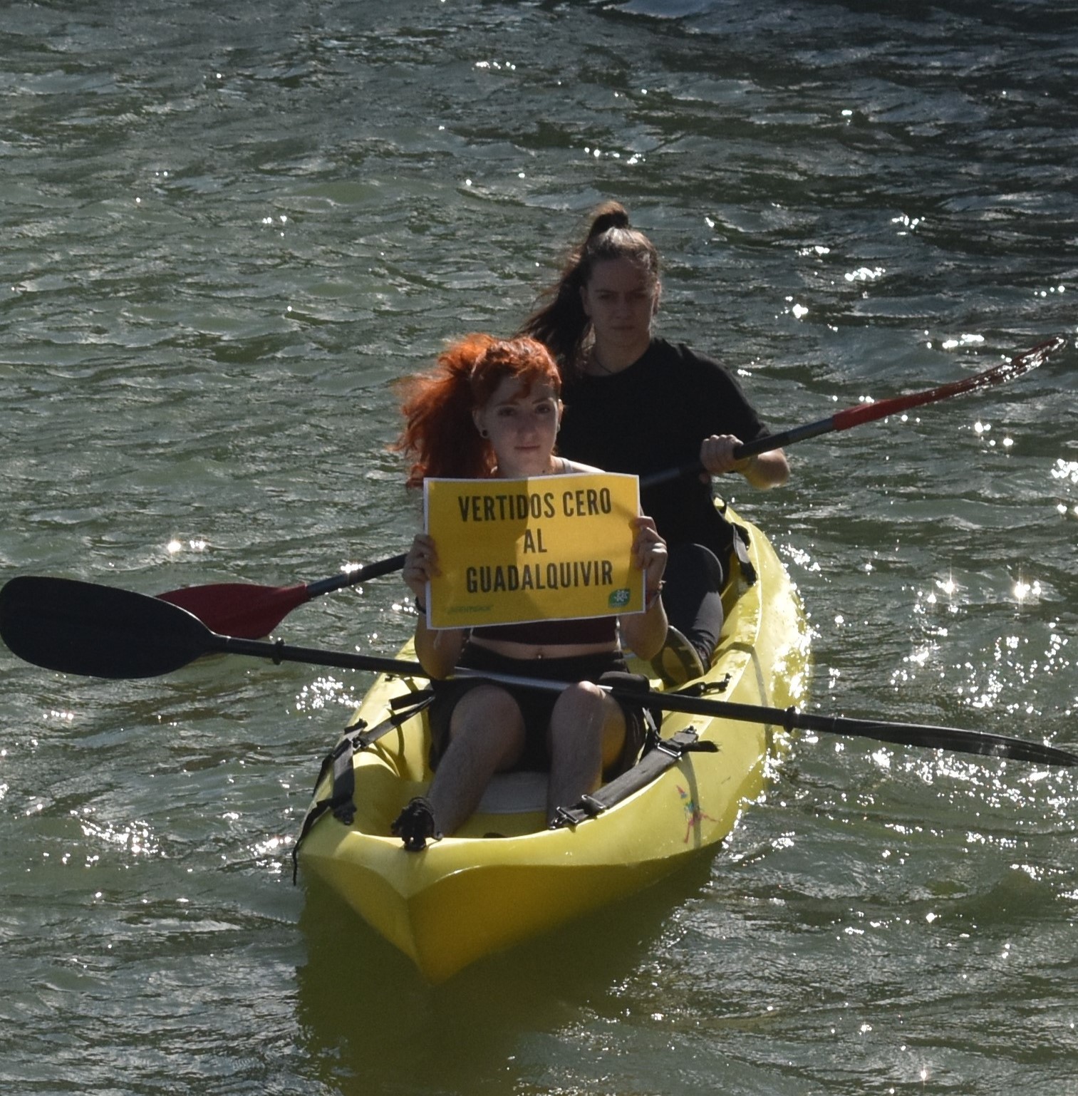 Dos chicas en barca portan el lema "No vertidos al Guadalquivir"